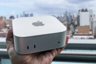 Mac mini M6 в ладони на фоне городской панорамы