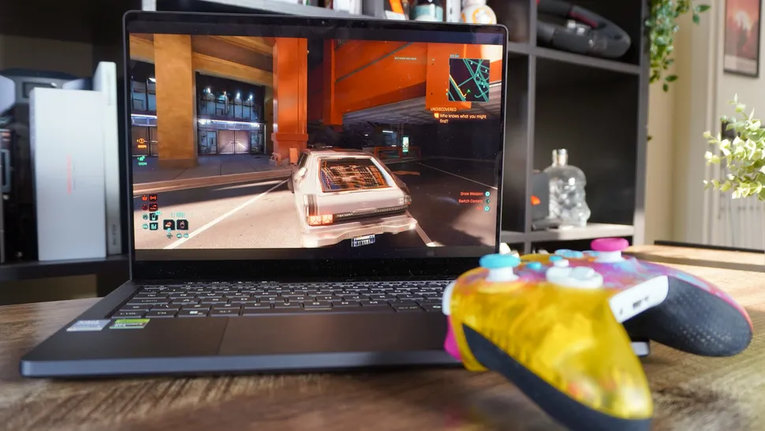 Asus ROG Zephyrus G14 2026 с запущенной игрой Cyberpunk 2077 на OLED-экране и геймпадом Xbox на переднем плане